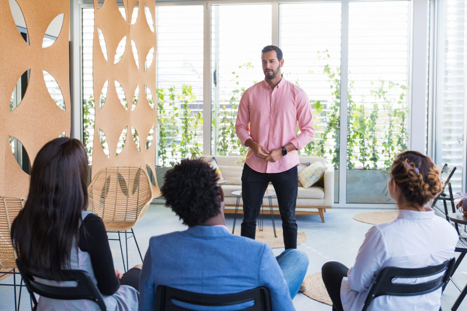 Man speaking to a group of three people in windowed room.